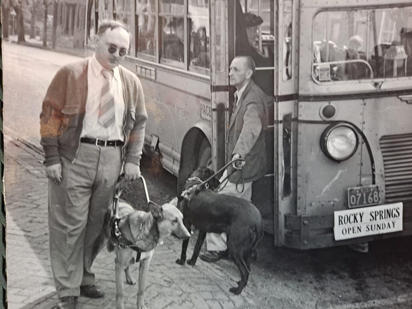 Two men holding squad dogs in front of the bus