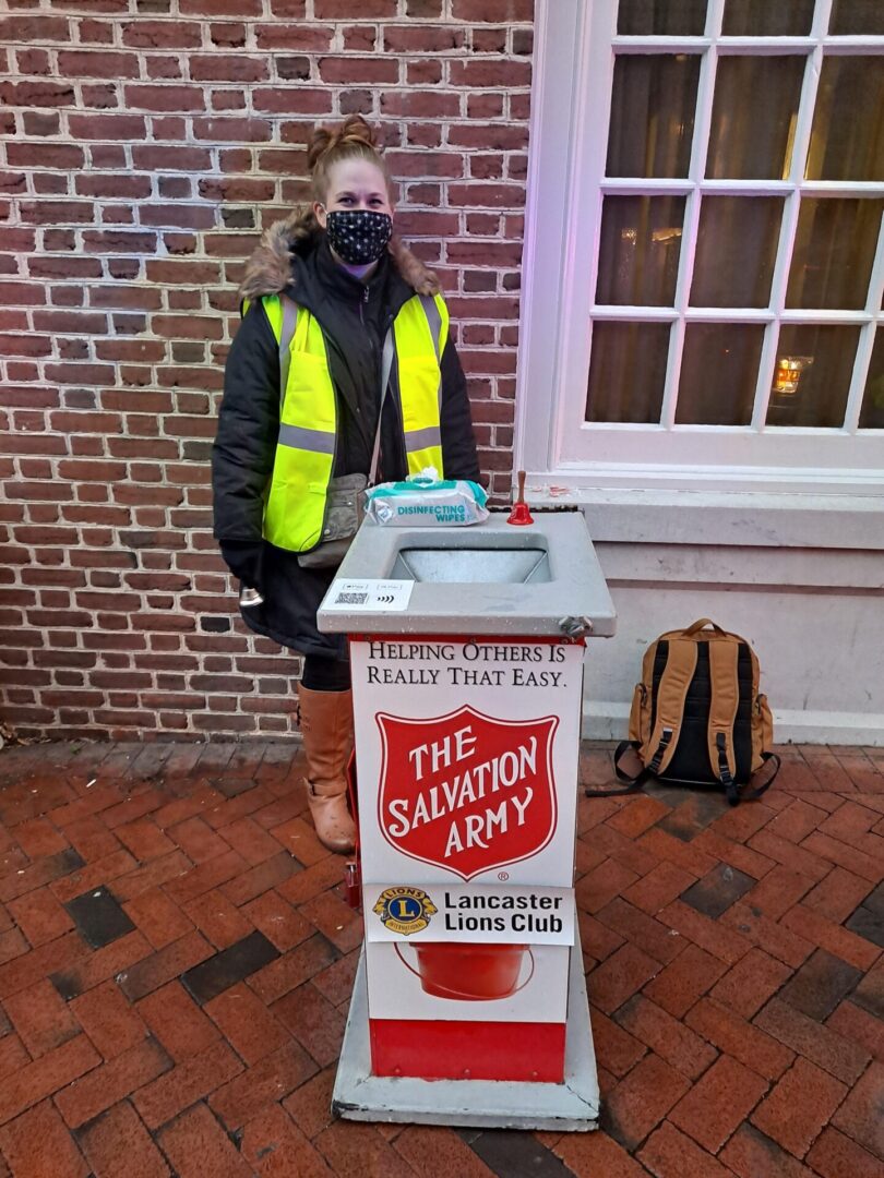 A woman in neon jacket standing behind salvation army box