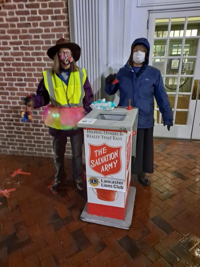 Two people wearing masks standing behind salvation box